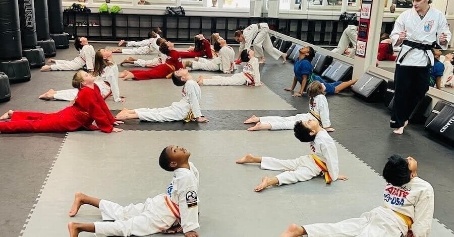 Kids martial arts class stretching during warm-up in training dojo